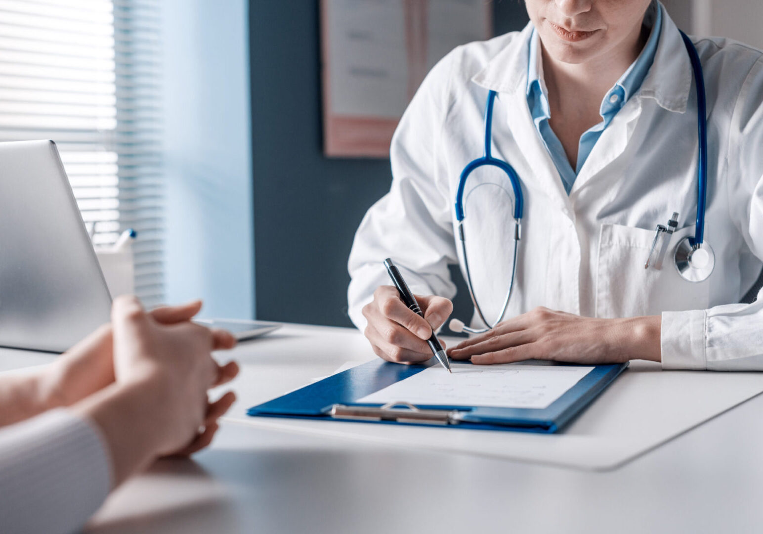 Doctor writing a medical prescription Doctor wearing a white coat and stethoscope writes on a clipboard during a consultation with a patient.