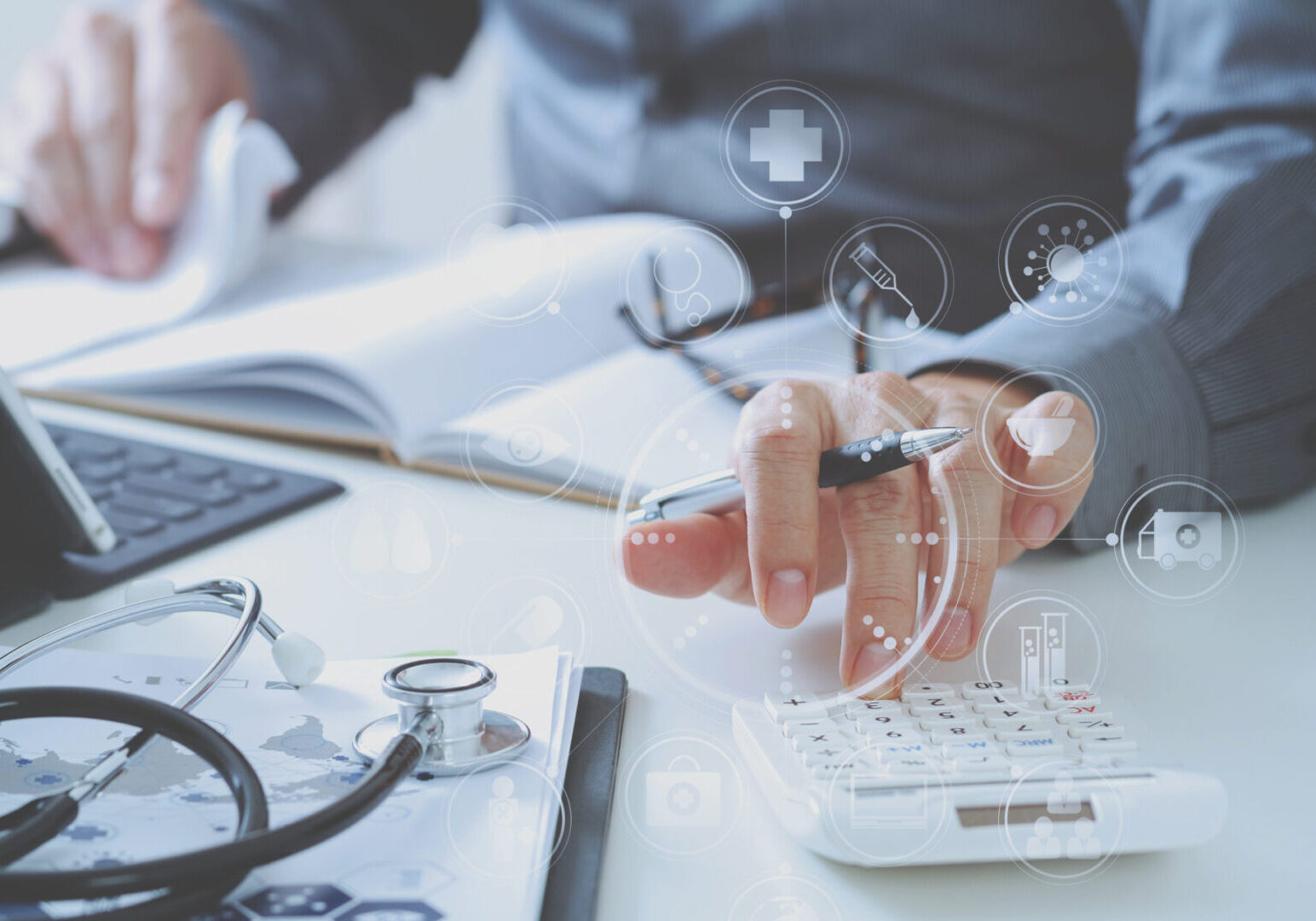 Healthcare costs and fees concept.Hand of smart doctor used a calculator for medical costs in modern hospital A person works at a desk with medical icons overlaying the image. They are using a calculator and holding a pen. Nearby are a stethoscope, clipboard, and an open book.